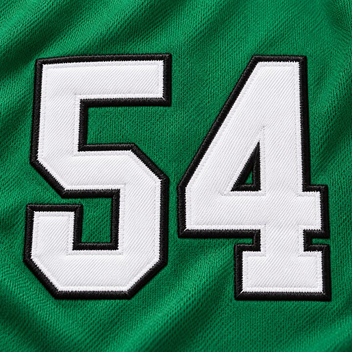 Close-up product mockup of white number 54 applique with raised black stitched borders on green jersey fabric.